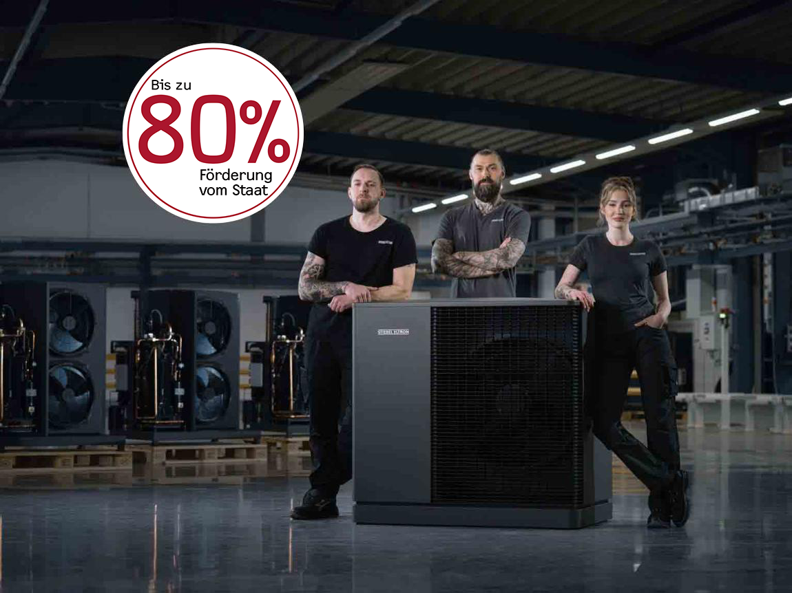 Das Bild zeigt zwei Wärmepumpe in weiß und anthrazit in einer Produktionshalle. Auf dem Bild ist zusätzlich der folgende Hinweis gegeben: Bis zu 80 % Förderung vom Staat.